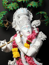 White Krishna idol close-up with gold flute and colorful flower garlands