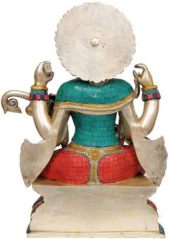 Brass Saraswati statue from behind, seated with raised hands and teal red patterned dress