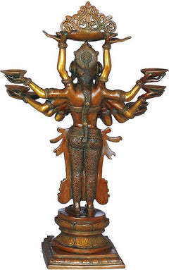 Antique brass-toned back view of ten-armed goddess statue with oil lamps on base.