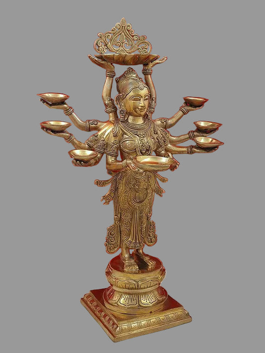 Brass ten-armed goddess statue with ornate crown and oil lamps, front three-quarter view.