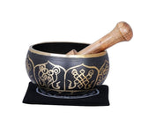 Brass singing bowl with black body and gold detailing; wooden mallet resting beside it