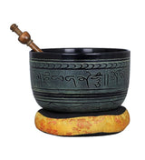 Brass singing bowl with black rim and green script, on golden cushion